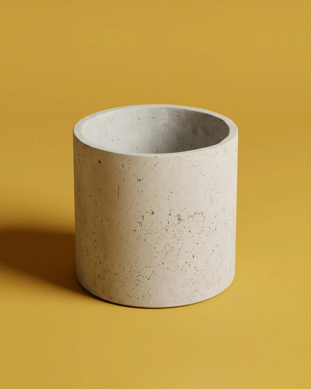 Maceta cilíndrica de concreto gris claro con poros visibles sobre fondo amarillo mostaza.