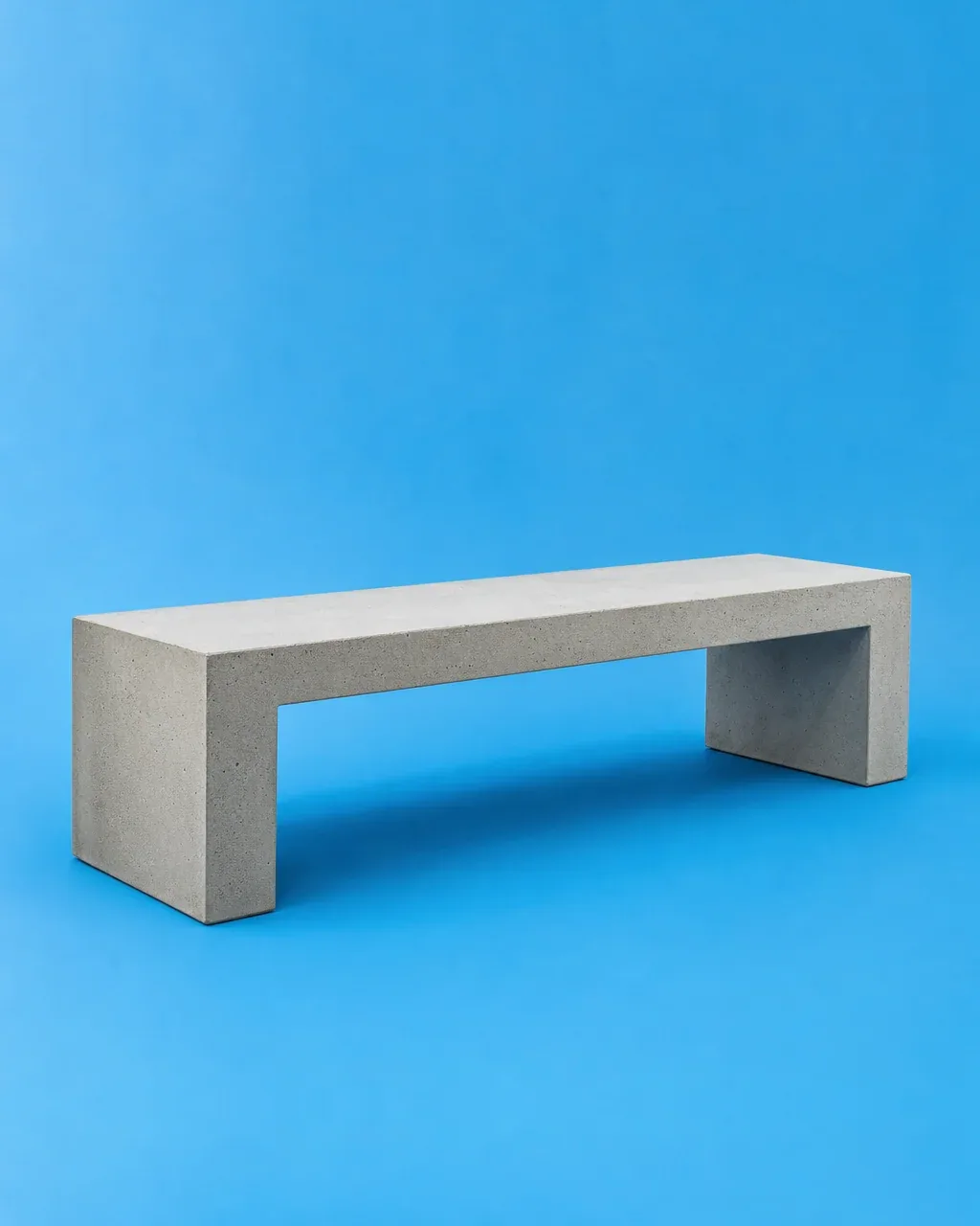 Banca de concreto gris claro de líneas rectas sobre fondo azul cielo.