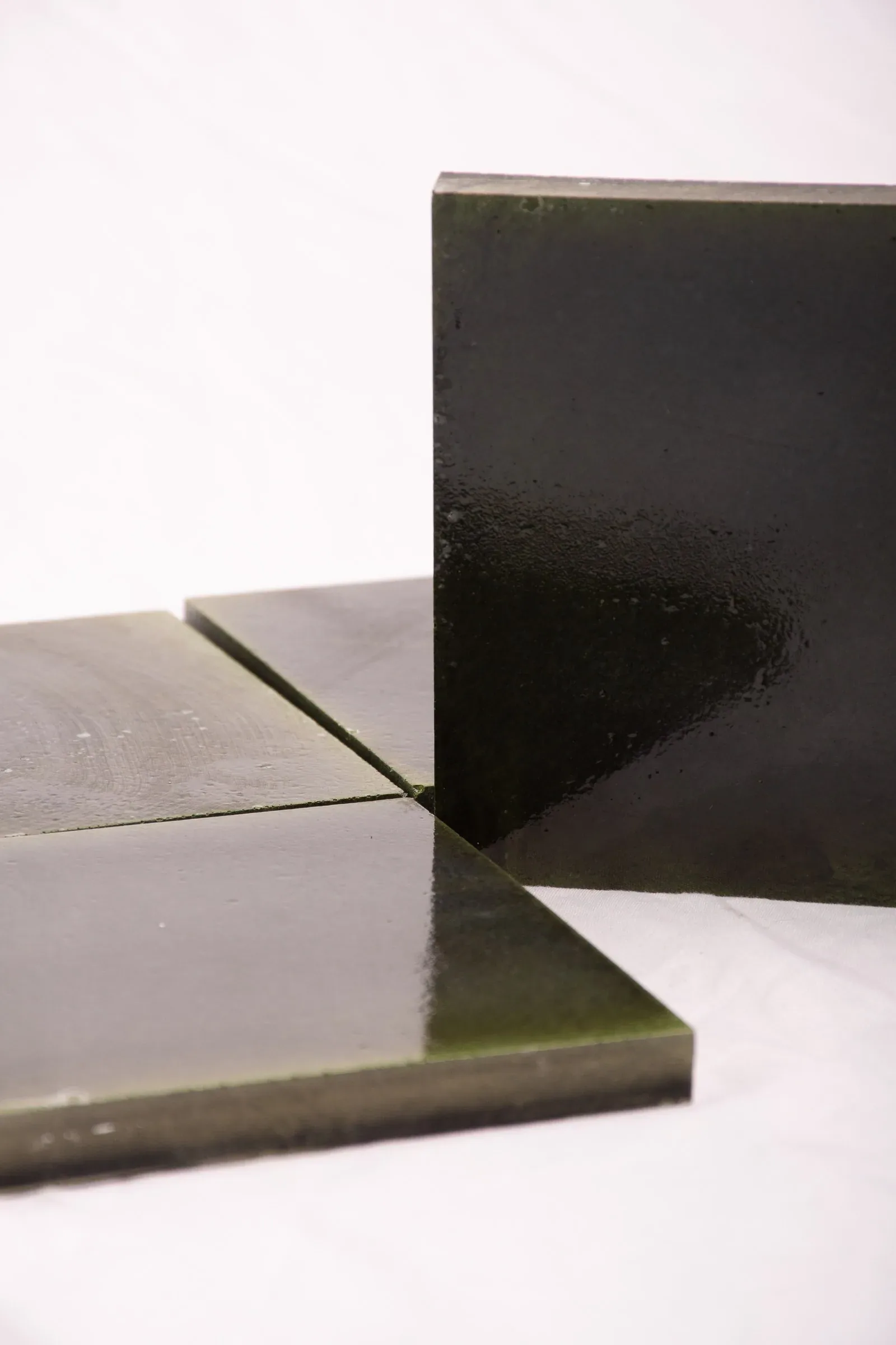 Losetas cuadradas de concreto verde oscuro sobre un fondo blanco.