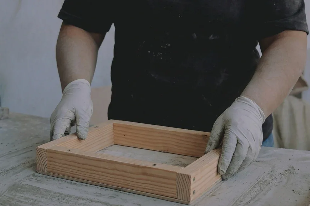 Manos con guantes preparando un molde en una mesa de trabajo.