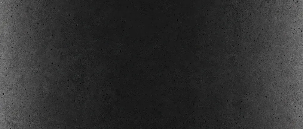 Superficie de concreto oscuro en penumbra, con poros sutiles y el centro en sombra.